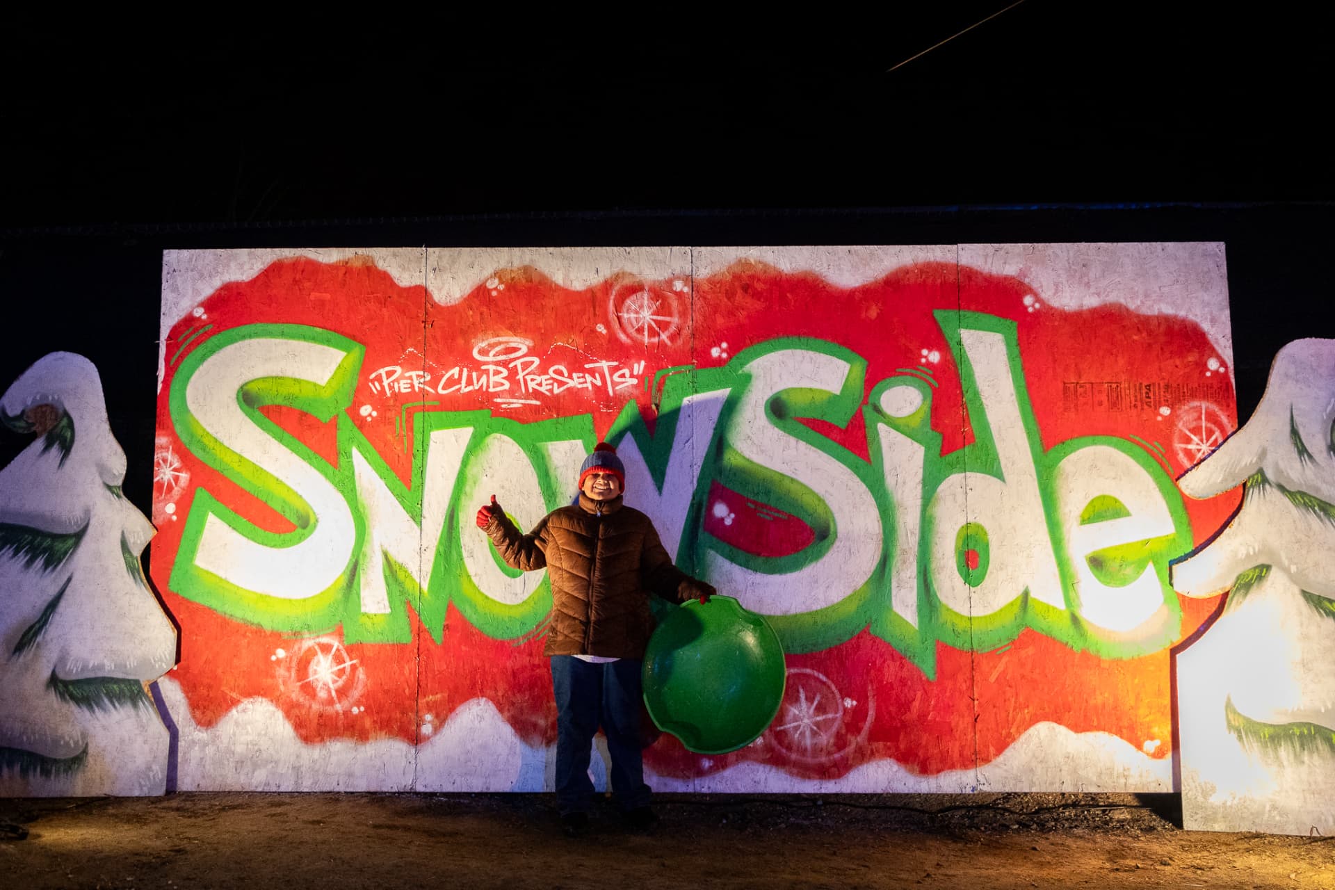 Guest with a sled in front of the painted SnowSide mural